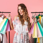 Photo_of_fashionable_girl_standing_in_store_near_clothes_rack_and_holding_colorful_shopping_bags_isolated_over_pink_background