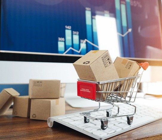 _E-commerce._Paper_boxes_in_shopping_cart_and_credit_card_on_keyboard_and_sales_data_economic_growth_graph_on_computer__screen,_online_shopping_and_payments,_banking,_buying_and_selling_services_online_on_network.