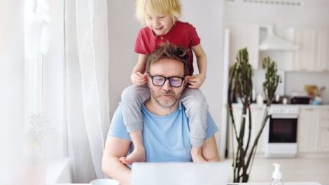 Man_working_from_home_with_laptop_during_quarantine._Home_office_and_parenthood_at_same_time._Exhausted_parent_with_hyperactive_child._Chaos_with_kids_during_isolation