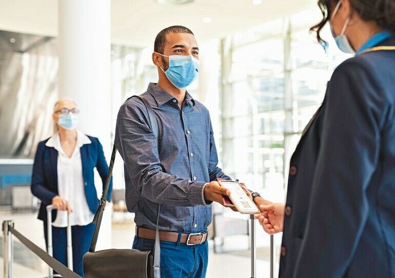 Indian_passenger_wearing_surgical_mask_showing_e-ticket_to_flight_attendant_at_boarding_gate._Young_mixed_race_businessman_showing_boarding_pass_on_mobile_phone_to_air_hostess_while_wearing_protective_face_mask_during_covid_pandemic._Multiethnic_business_