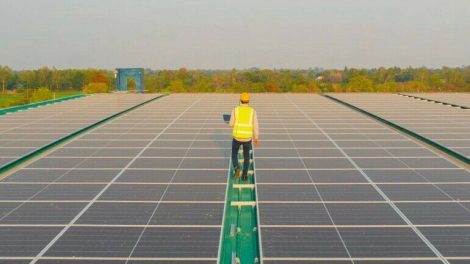 Aerial_top_view_of_engineer_man_or_worker,people,_with_solar_panels_or_solar_cells_on_the_roof_in_factory_industry._Power_plant,_renewable_energy_source._Eco_technology_for_electric_power._Maintenance