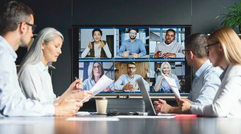 Global_corporation_online_videoconference_in_meeting_room_with_diverse_people_sitting_in_modern_office_and_multicultural_multiethnic_colleagues_on_big_screen_monitor._Business_technologies_concept.