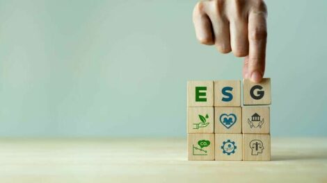 ESG_concept_of_environmental,_social_and_governance._Sustainable_corporation_development._Hand_holds_wooden_cubes_with_abbreviation_ESG_standing_with_other_ESG_icons_on_grey_background._Copy_space.