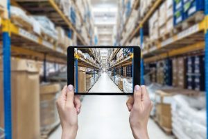 Horizontal_color_image_of_female_hands_holding_a_digital_tablet_in_a_corridor_of_futuristic_distribution_warehouse._Ordering_on-line_from_a_modern_warehouse_on_a_touchscreen_tablet_computer._Large_distribution_storage_in_background_with_racks_full_of_pack