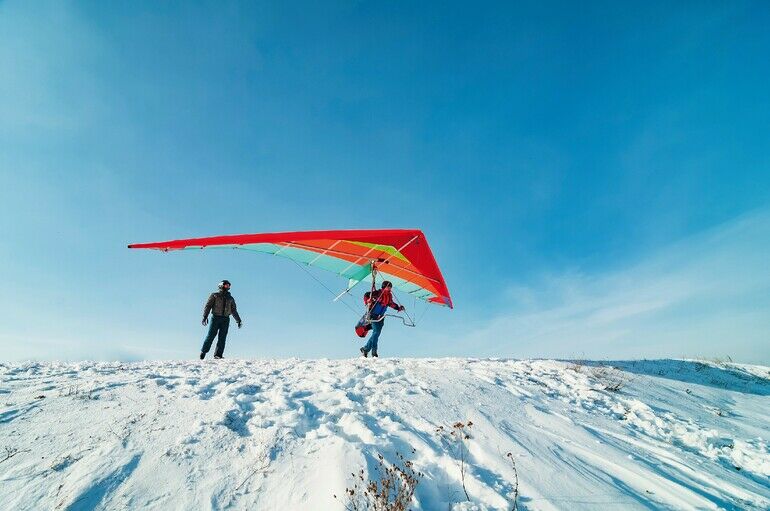 Hang_glider_pilot_ready_to_take_off_from_mountain_withhis_bright_wing._Other_pilot_is_looking_at_him._Extreme_aerial_sport.