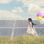 A_funny_girl_carrying_a_colorful_balloon_running_in_a_meadow_with_a_Solar_panel,_photovoltaic._Concept_of_Eco-Friendly_,Clean_Energy_,_Pure_energy_and_Sustainable_energy